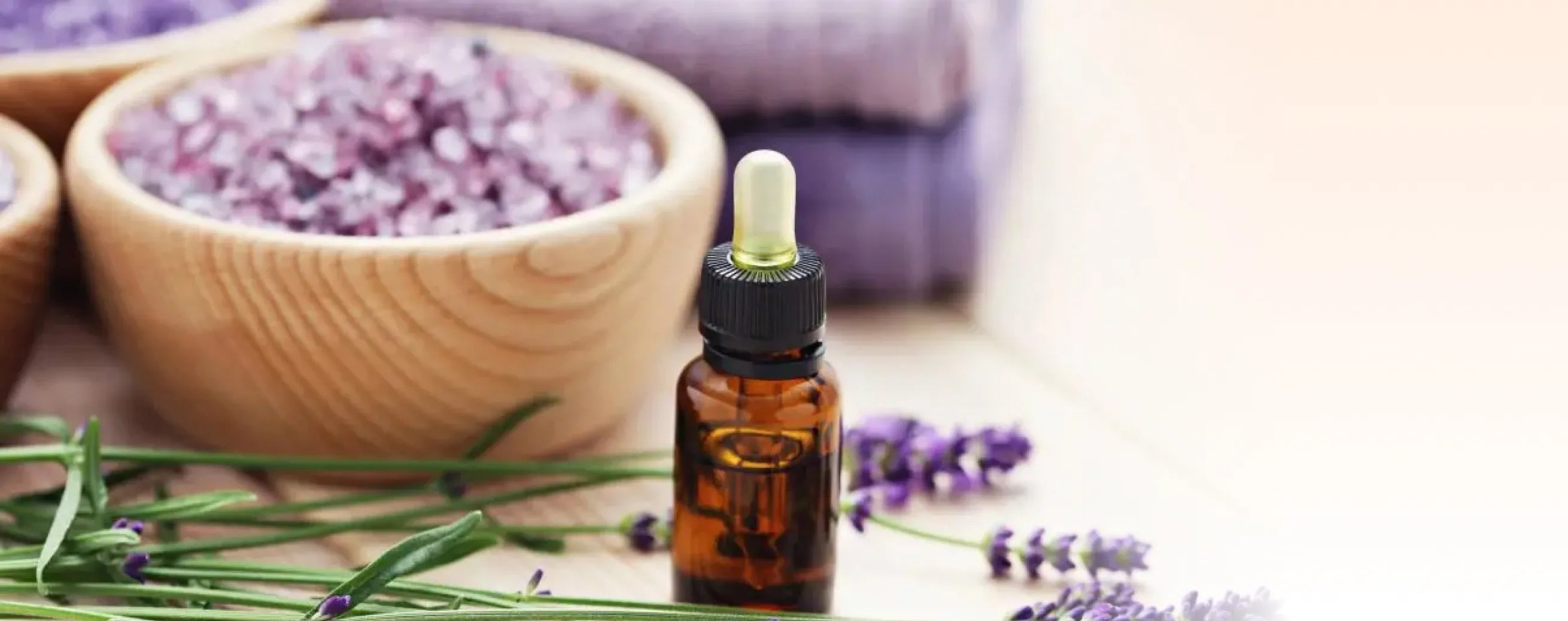 Bottle of essential oil with lavender flowers and bowls of lavender petals on a wooden surface