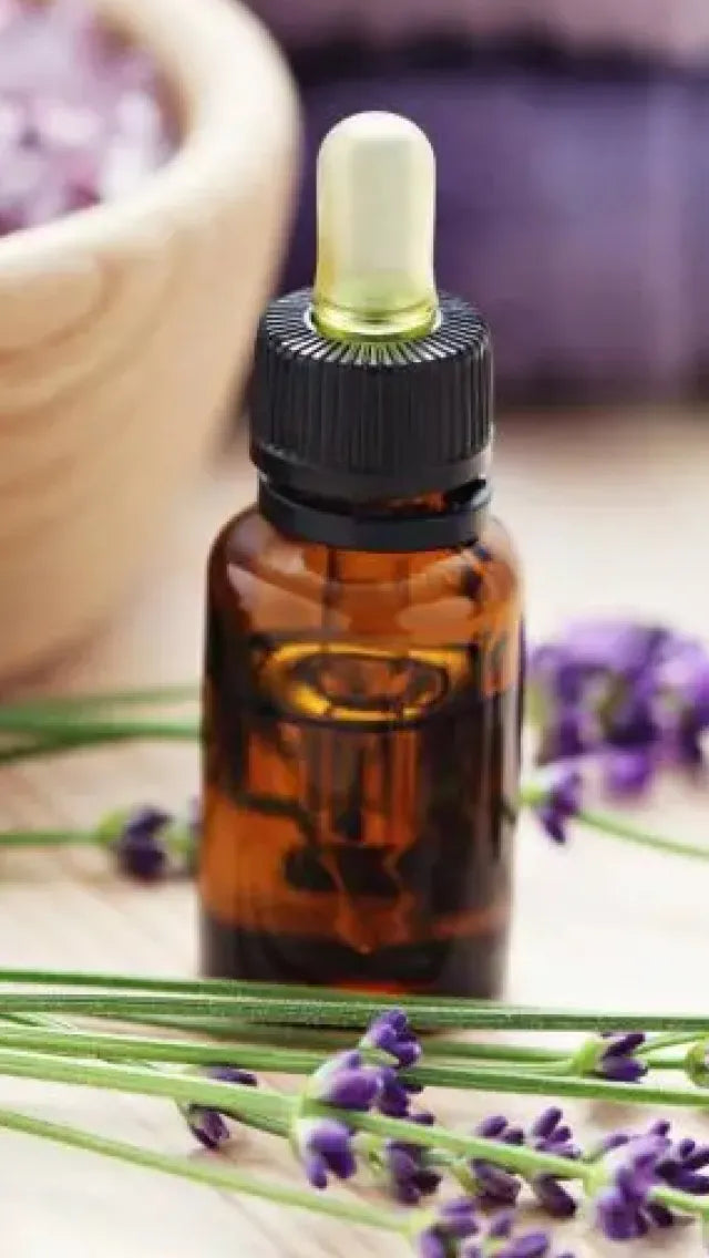 Brown dropper bottle with black cap on a wooden surface with lavender flowers.